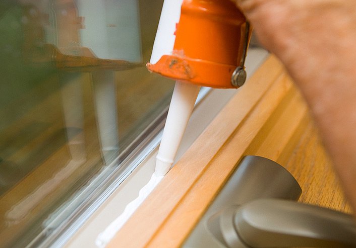 close up picture of a caulk gun on a window sealing a window air leak 
