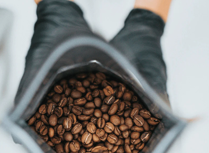 A black handed gloves holding a packs of coffee beans