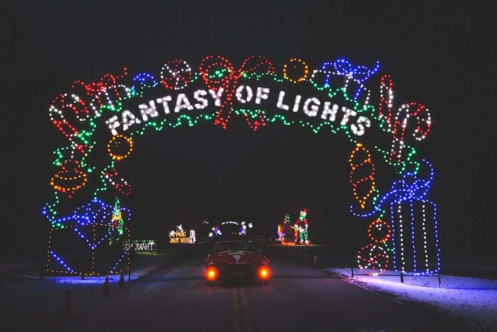 arch with holiday lights over the road and a car driving down it 